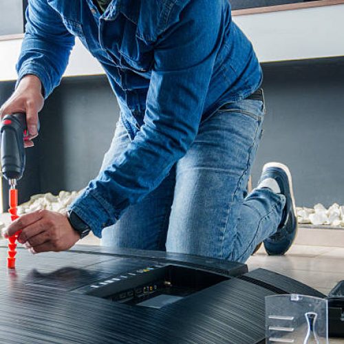 Professional technician using electric screwdriver repairing smart tv at home
